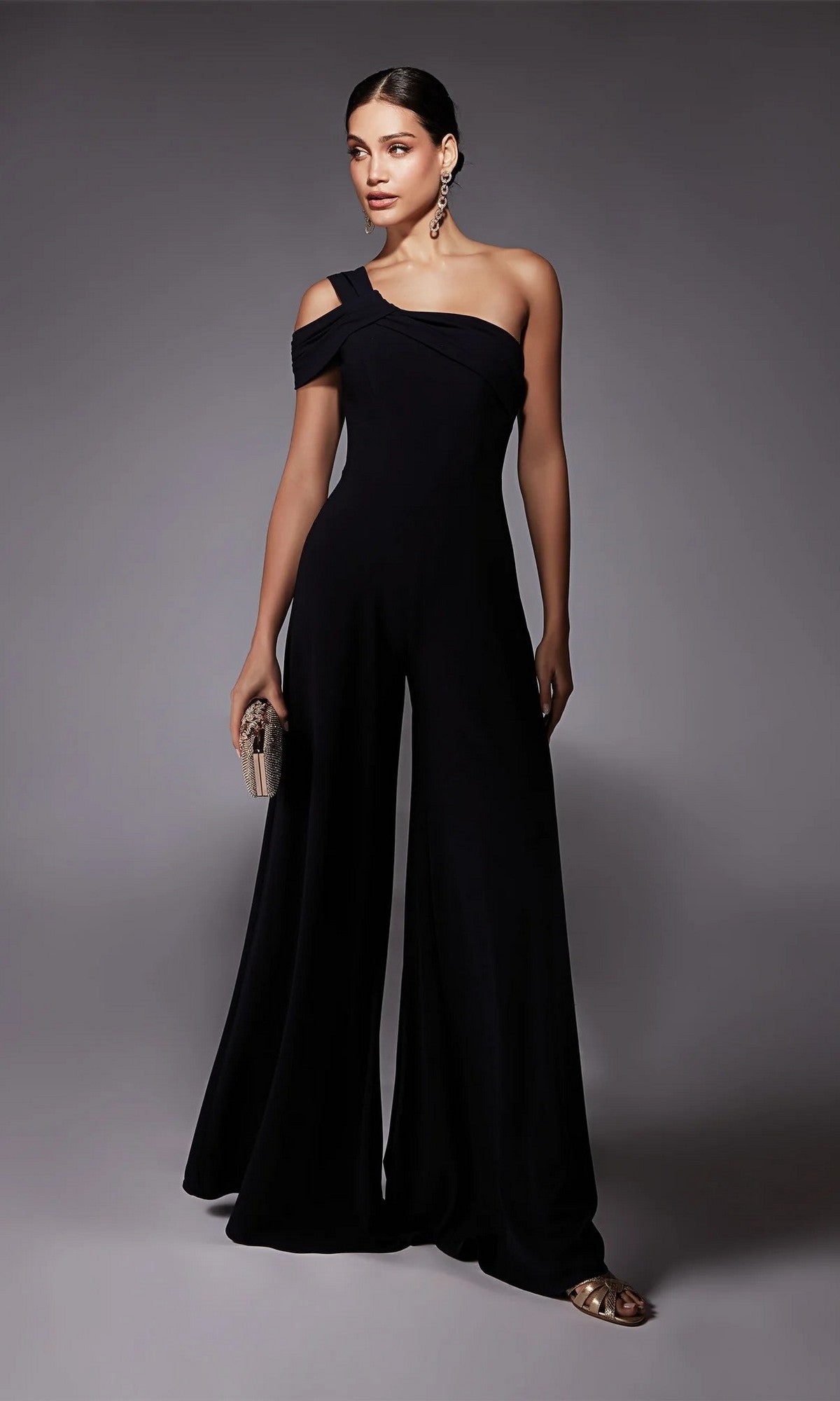 A woman poses against a plain gray background in the Alyce 70066 Long Formal Jumpsuit, featuring a one-shoulder design and wide-leg pants. She accessorizes with earrings and holds a small clutch.